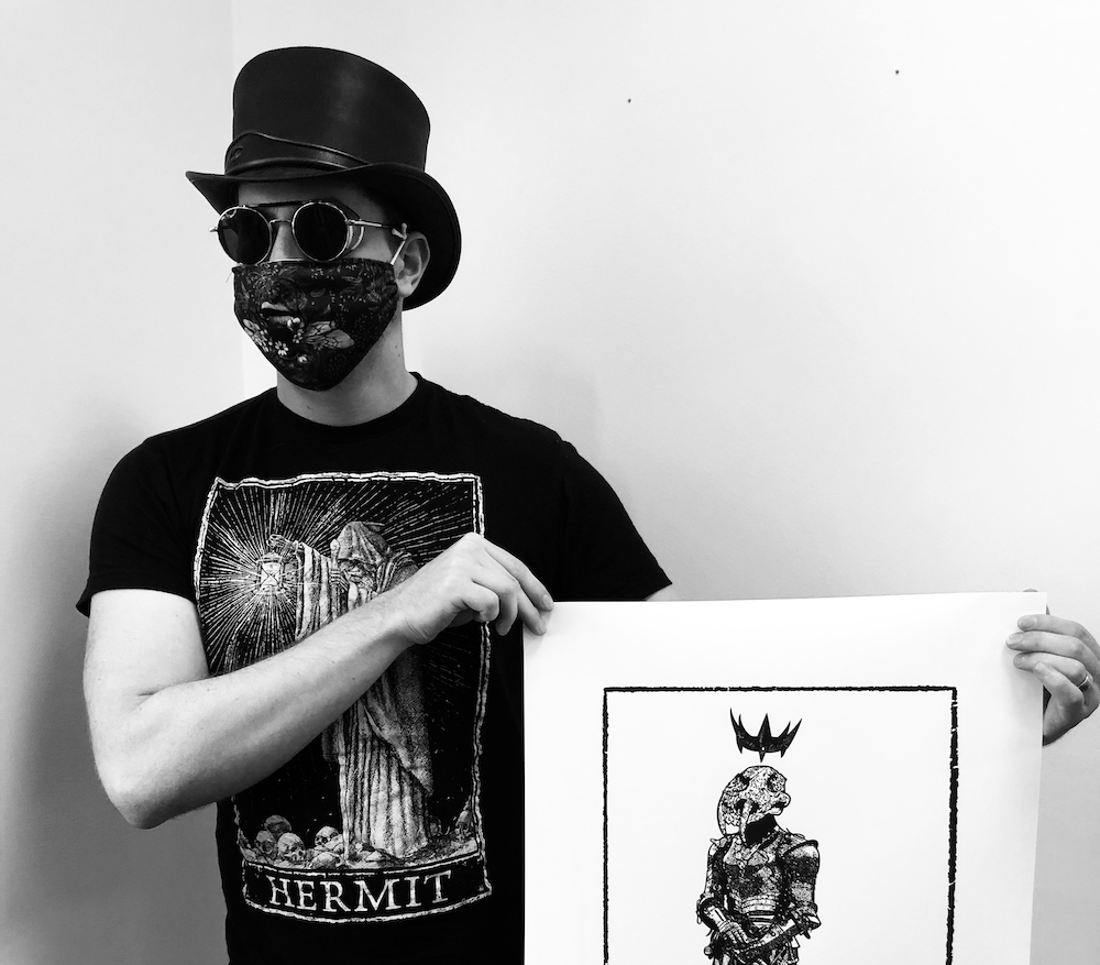 photo of artist in top hat, sunglasses, and mask, with a print t-shirt holding his own print